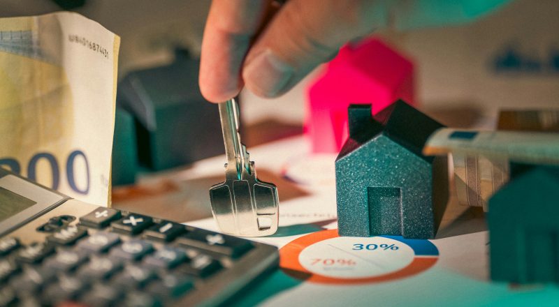 A close-up of real estate financial planning with keys, calculator, and money.